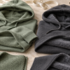 Sage green and charcoal hoodies with exposed loopback and brushed interiors beside matching fabric swatches.